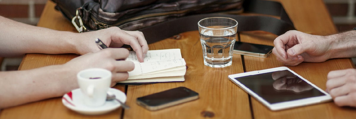 Ihmiset kirjoittavat muistiinpanoja kahvilassa, pöydällä tabletti ja puhelimia