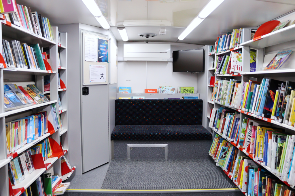 Kirjastoauton peräosan lasten ja nuorten osasto. Kirjahyllyjä ja istuin.