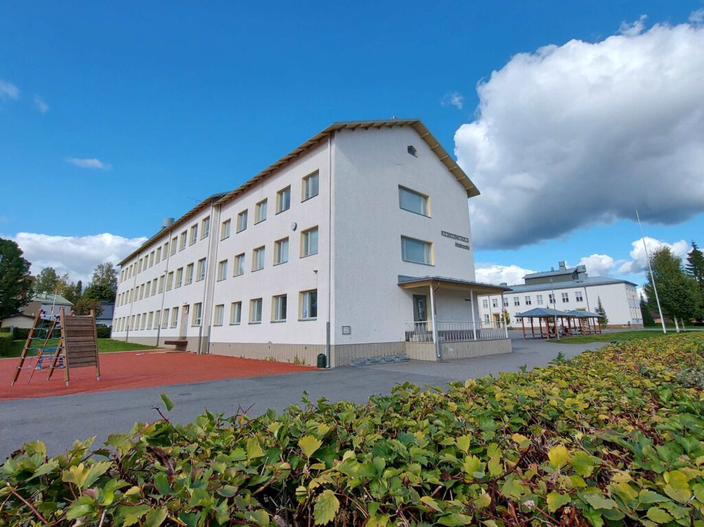 Koulun piha-alue. Kaksi kivirakennusta, pyöräkatokset ja leikkialue.