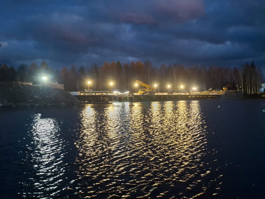 Siltatyömaa valaistuna työvaloilla illan hämärässä. Työsillan päällä nosturi. Lokakuu 2025.