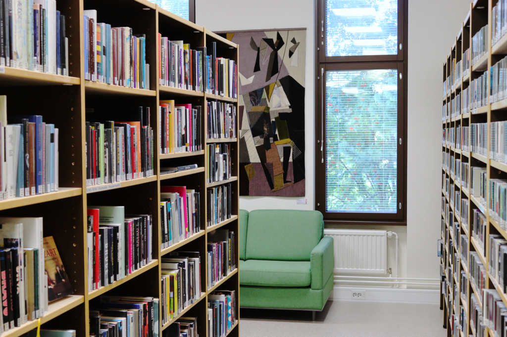 Kirjaston musiikkiosasto. Molemmilla sivuilla näkyy kirja- ja levyhyllyjä, keskellä sohva ja ikkuna. Ikkunan vieressä seinällä on tekstiilitaideteos.