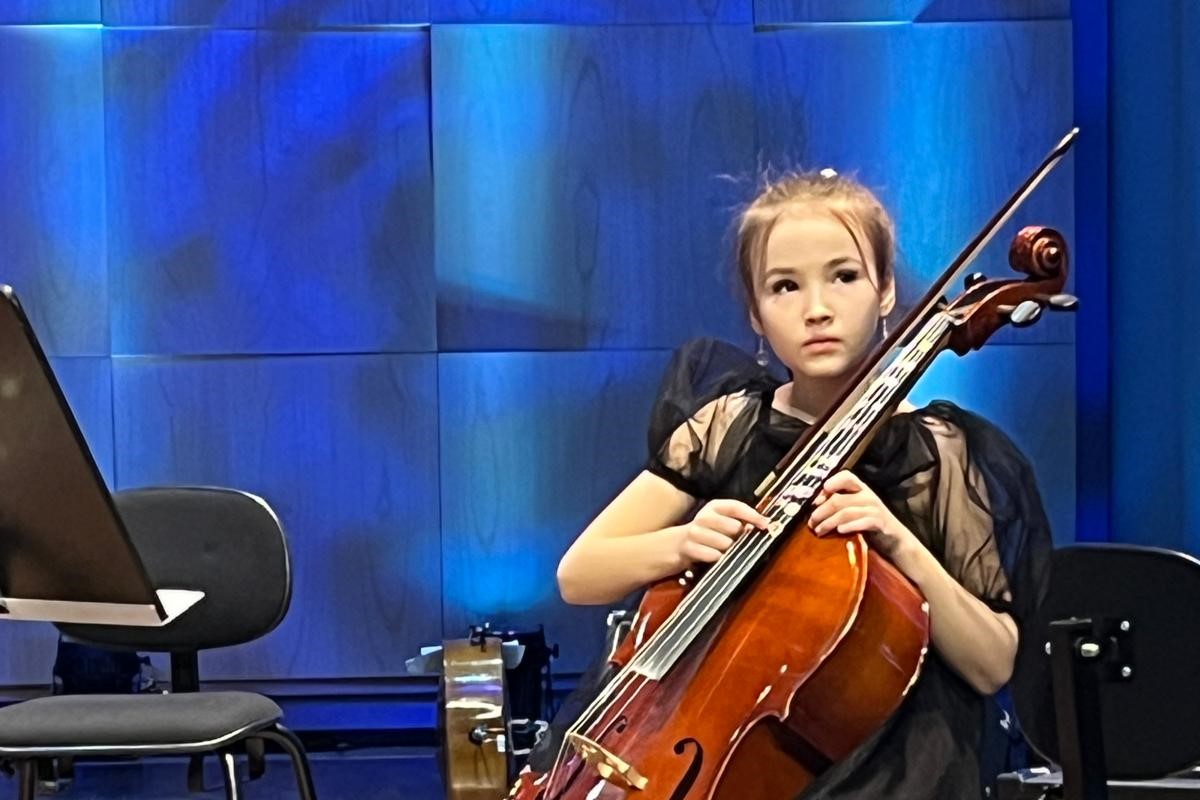 Tyttö soittamassa selloa esiintymislavalla. Soittaja katsoo yleisöön päin.