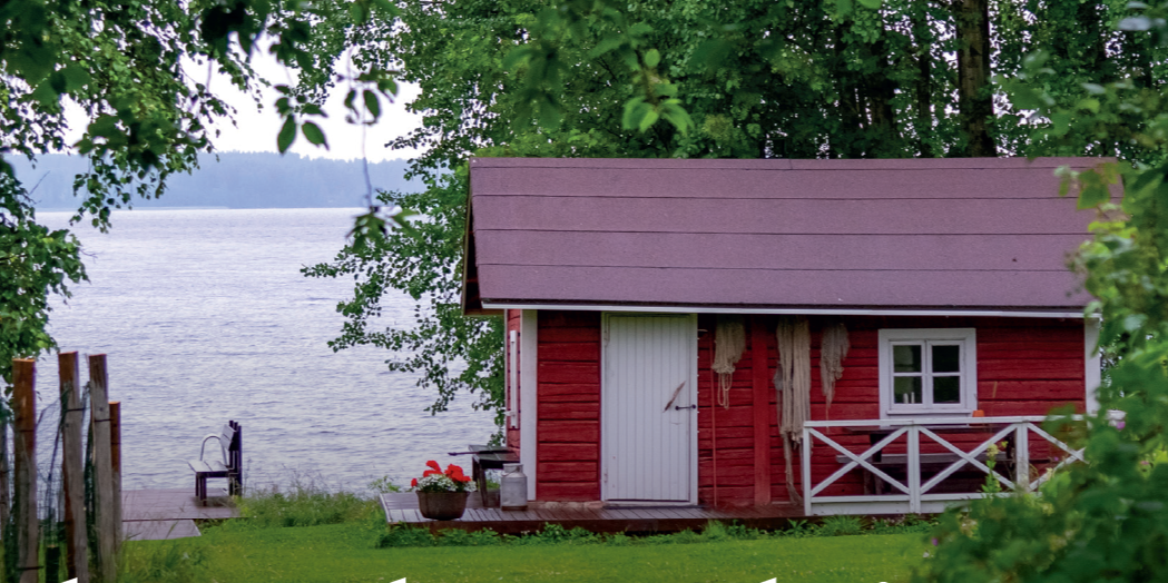Punainen saunamökki järven rannalla.